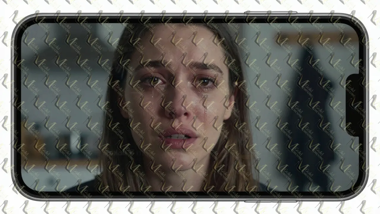 Кадр из видео на экране телефона: женщина говорит прямо в камеру, на лице — тишина и слезы, за ней — размытая кухня и вешалка с пальто.